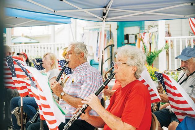 Members of a community band play music they are reading from music stands painted to look like American flags.
