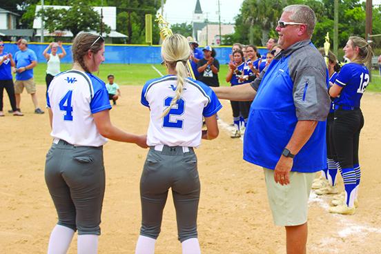 Peniel Baptist Academy softball coach Jeff Hutchins hands the Florida Christian Athletic League trophy to senior members Rylee Romay (4) and Brook Williams after winning the title on April 29 at Rotary Park against Gainesville Countryside Christian. (MARK BLUMENTHAL / Palatka Daily News)
