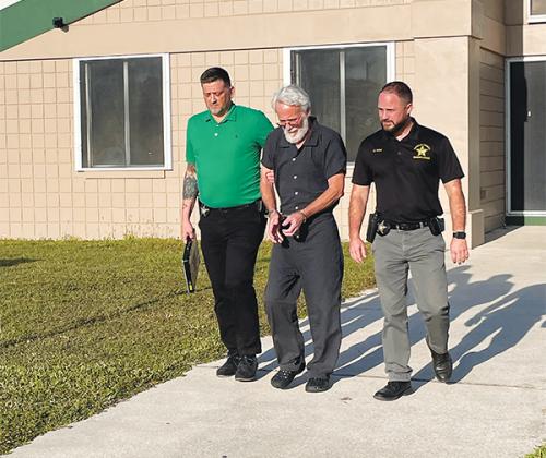 Photo courtesy of the Putnam County Sheriff's Office – Peter Miles Hamilton, 66, center, is walked into the Putnam County Jail to be booked on the charge of murdering his wife.