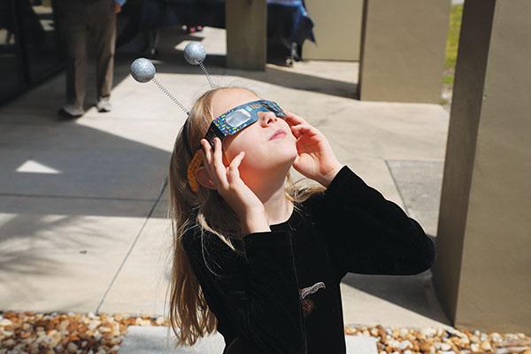 Photo submitted by Susan Kessler – A little girl wearing even littler moons on her headband looks at the eclipse at SJR State.
