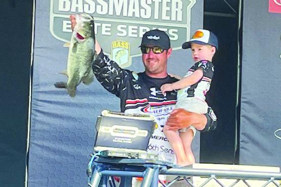 With his son, Luke, in his left arm, Cory Johnston holds up one of his five fish he caught Saturday to maintain the lead going into the final round Sunday of the MAXAM Bassmaster Elite at the St. Johns River. (MARK BLUMENTHAL / Palatka Daily News)