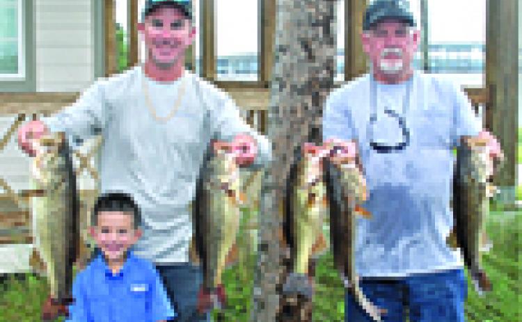 Justin Atkinson, left, and Brett Bollinger hold up their winning fish on Saturday. Conner Atkinson, Justin’s son, joins in the festivities. (GREG WALKER / Special To The Daily News)