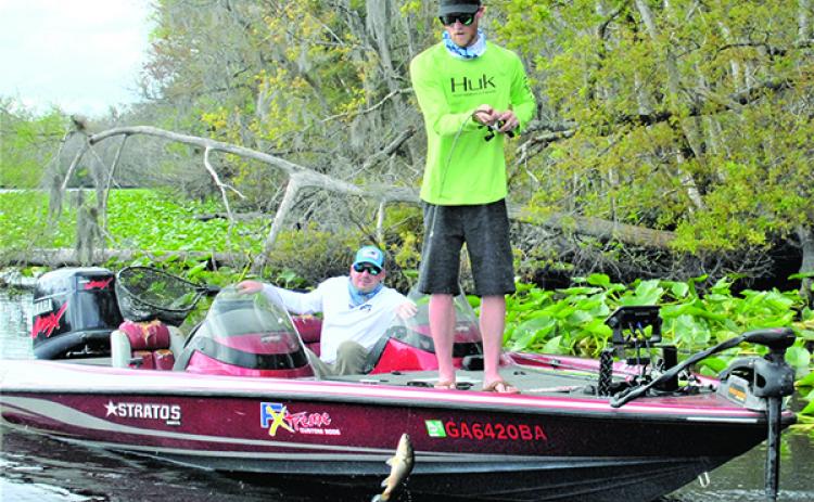 Byron Hendrix of Atlanta (standing) boats a bass on the final day of pre-fish, while flipping a jig in the lily pads. Brad Cassals (sitting) of Washington, D.C., is observing. (GREG WALKER / Special To The Daily News)