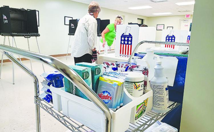 A cart filled with sanitizing products is stationed in the Supervisor of Elections Office on Friday while election clerks Claudia Wilkinson and Vicky Dennis set up for early voting.