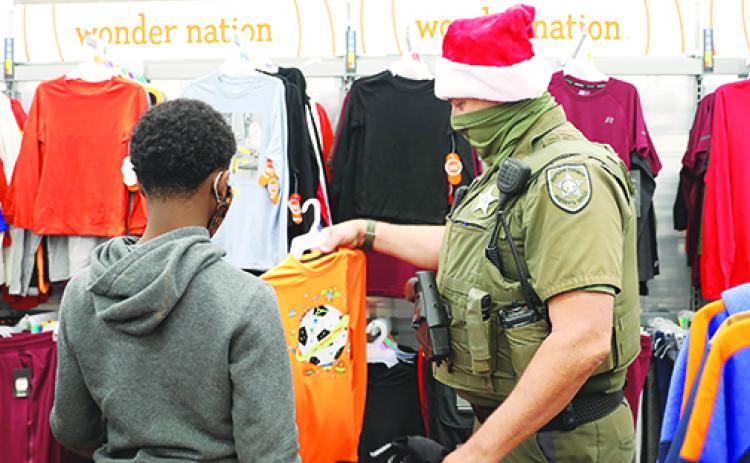  A Putnam County Sheriff’s Office deputy helps a local child pick out clothes for Christmas on Sunday as part of the second annual Shop with a Deputy, where the agency partners with the Guardian ad Litem program to make sure children in foster care have gifts for Christmas. 