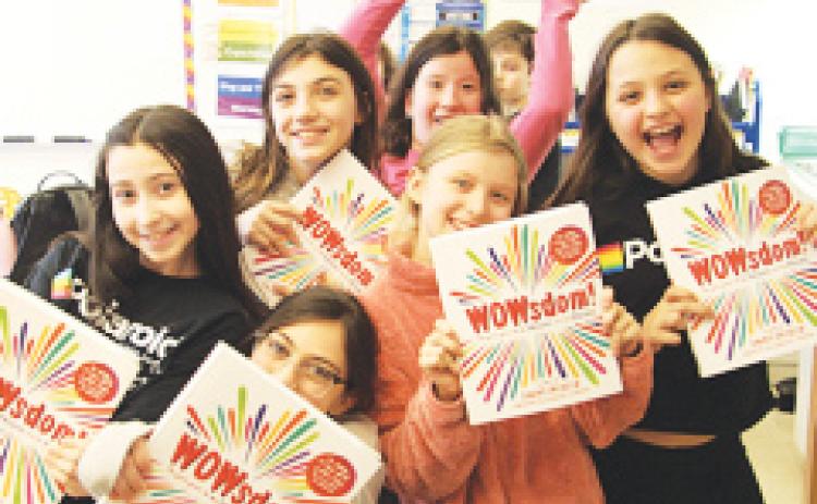 Girls smile and hold the book “WOWsdom!,” written by Generation W founder Donna Orender, that teachers leadership and self-esteem.