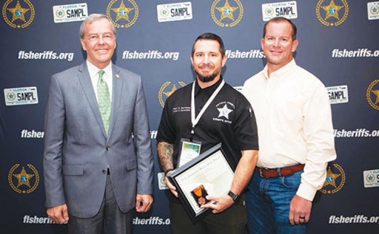 At the Florida Sheriff’s Association Summer Conference on Tuesday, Collier County Sheriff Kevin Rambosk, left, and Putnam County Sheriff Gator DeLoach, right, present Putnam County Sheriff’s Office Maj. Scott Surrency with an award for administering CPR to a woman struck by lightning on a Naples beach the day before.