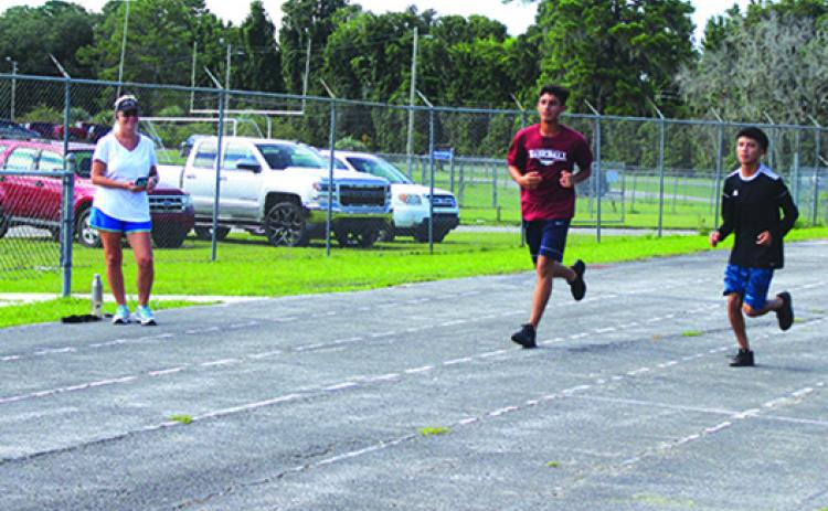 Jesus Cruz (middle) and Anthony Vazquez do laps on the Crescent City track during practice last month as longtime Crescent City cross country coach Jen Ewbank looks on. The program returns this year after being gone in 2020. (MARK BLUMENTHAL / Palatka Daily News)
