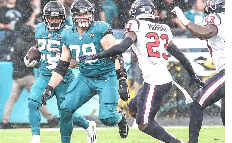Jaguars running back James Robinson (25) dashes in between raindrops for yardage as teammate and lineman Ben Bartch leads the way in front of Texans defender Eric Murray. (JOHN STUDWELL / Special to the Daily News)