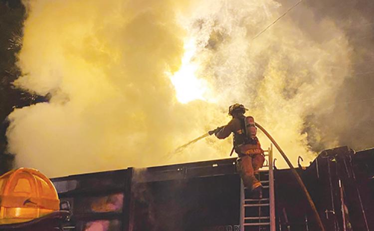 A firefighter stands atop a ladder as he attempts to put out the blaze that erupted in a Palatka garbage truck.