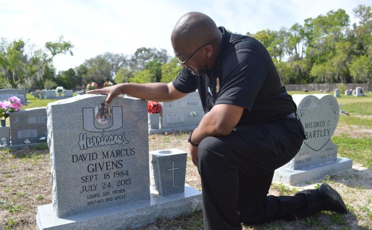 Casmira Harrison/Palatka Daily News Anterio Smith rubs some dirt off a photo of his little brother and his brother’s children that adorns David Marcus Givens’ grave. Smith, who works in the medical examiner's office that oversees Putnam County deaths, wants his brother’s killers brought to justice and to see fewer familiar faces in the morgue.