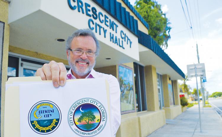 Charles Rudd, city manager for Crescent City, is seen in front of City Hall on Friday holding up the city’s outgoing logo, left, and the new city seal, right, commissioners approved this week.