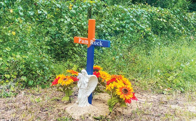 An orange and blue cross, new flowers and an angel sit on the side of Walker Drive in Interlachen to honor Pam Rock, who died a day after she was attacked by five dogs on that street last month.