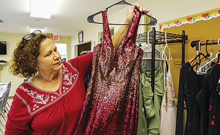Whispering Hope Church of God member Wanda Strickland holds up a red and gold sequined dress that was donated to the church and is available for girls to wear for free to their homecoming or prom.