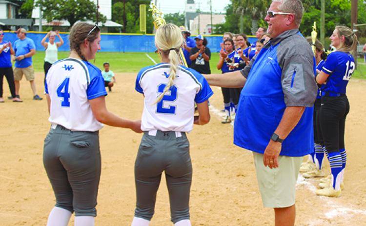 Peniel Baptist Academy softball coach Jeff Hutchins hands the Florida Christian Athletic League trophy to senior members Rylee Romay (4) and Brook Williams after winning the title on April 29 at Rotary Park against Gainesville Countryside Christian. (MARK BLUMENTHAL / Palatka Daily News)