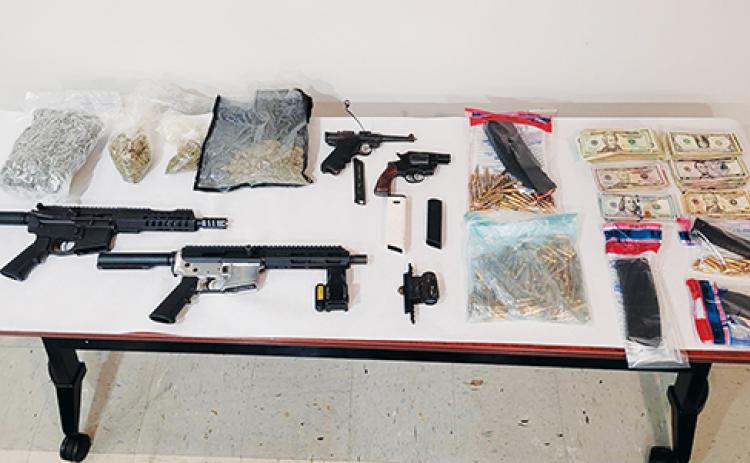 Photo courtesy of the Palatka Police Department – A table full of guns, ammunition, drugs and cash are on display after Palatka Police Department officers confiscated them as evidence from an Eagle Street house.